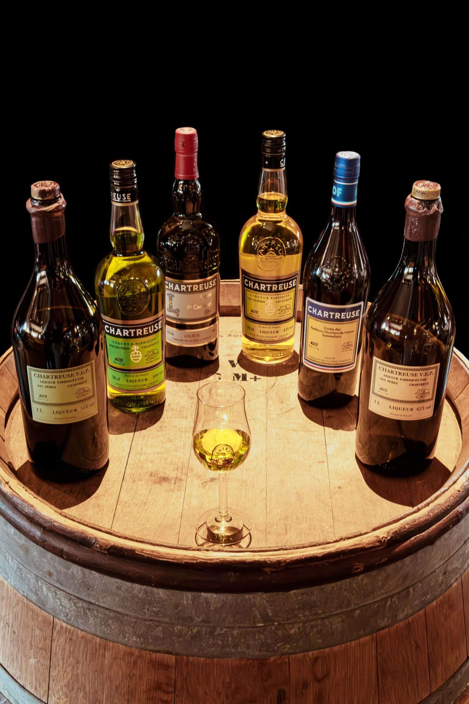 Une collection de liqueurs Chartreuse, emblème de la région, présentée sur un tonneau pour une dégustation authentique en Haute-Savoie.