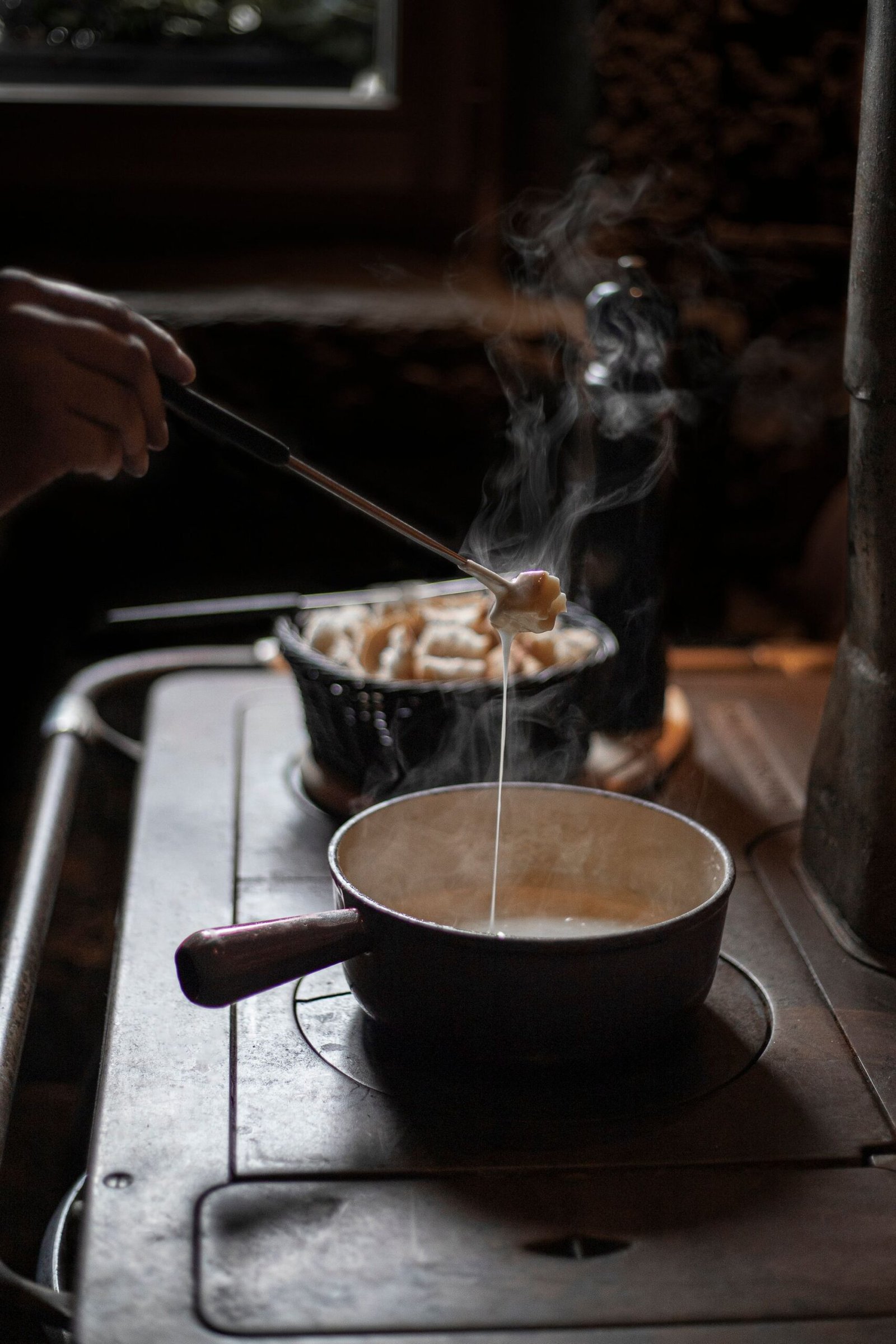 Un moment capturé de la préparation d'une fondue savoyarde traditionnelle, avec du fromage fondu et des morceaux de pain, une spécialité de notre restaurant haut-savoyard.